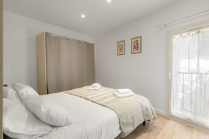 A bedroom with a bed, a window with curtains, and two framed pictures on the wall. - Apt L’Hospital – In the heart of Tourrettes-sur-Loup (Tourrettes-sur-Loup)