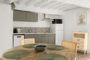 A modern kitchen with a dining area, featuring a round table with a bowl, chairs, and a microwave above the counter. - Apt L’Hospital – In the heart of Tourrettes-sur-Loup (Tourrettes-sur-Loup)