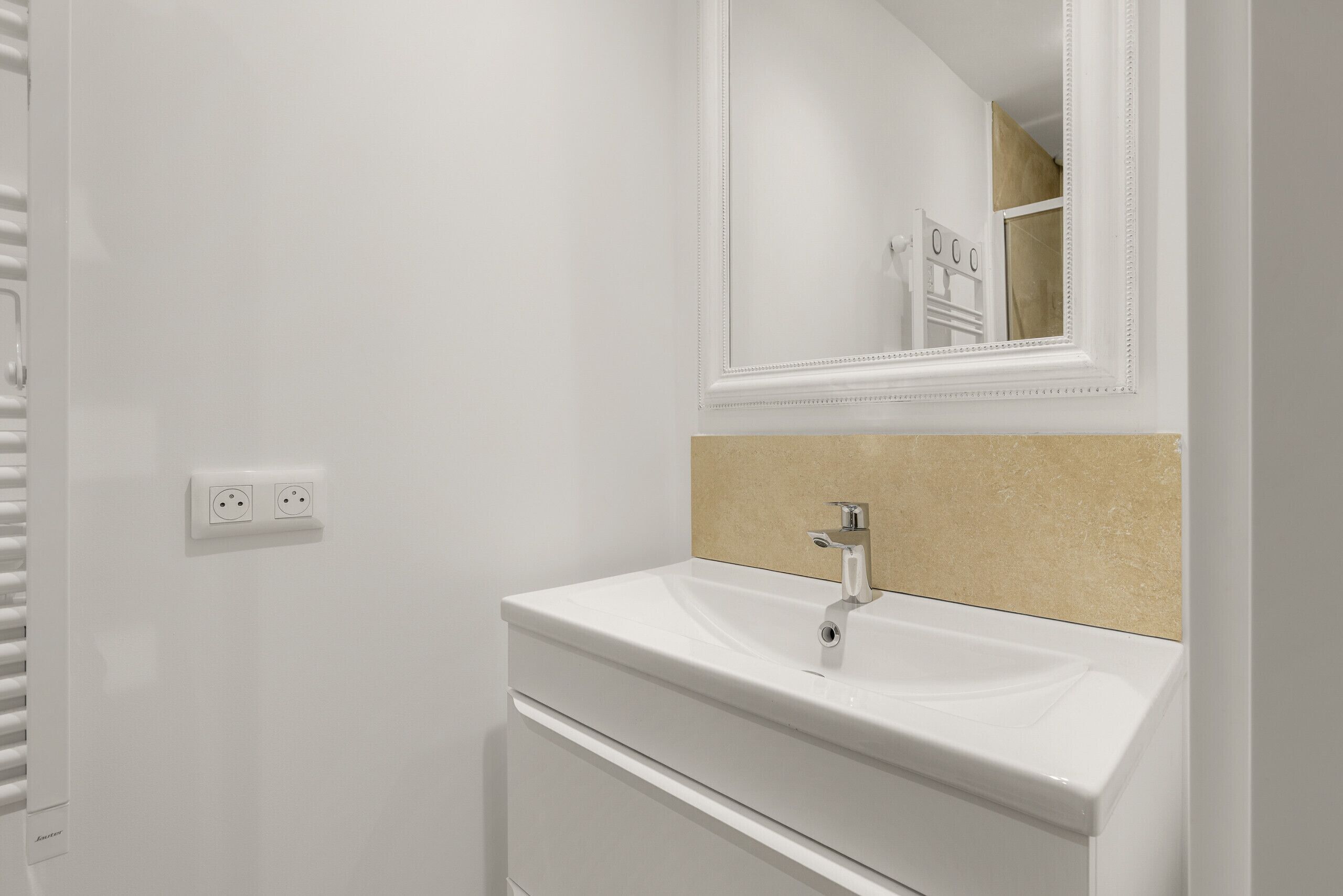 A bathroom with a white sink, a mirror, and a beige countertop.