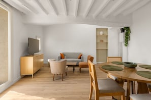 A modern living space with a wooden dining table, chairs, a grey sofa, a television on a wooden cabinet, and a plant on the wall. - Apt L’Hospital – In the heart of Tourrettes-sur-Loup (Tourrettes-sur-Loup)