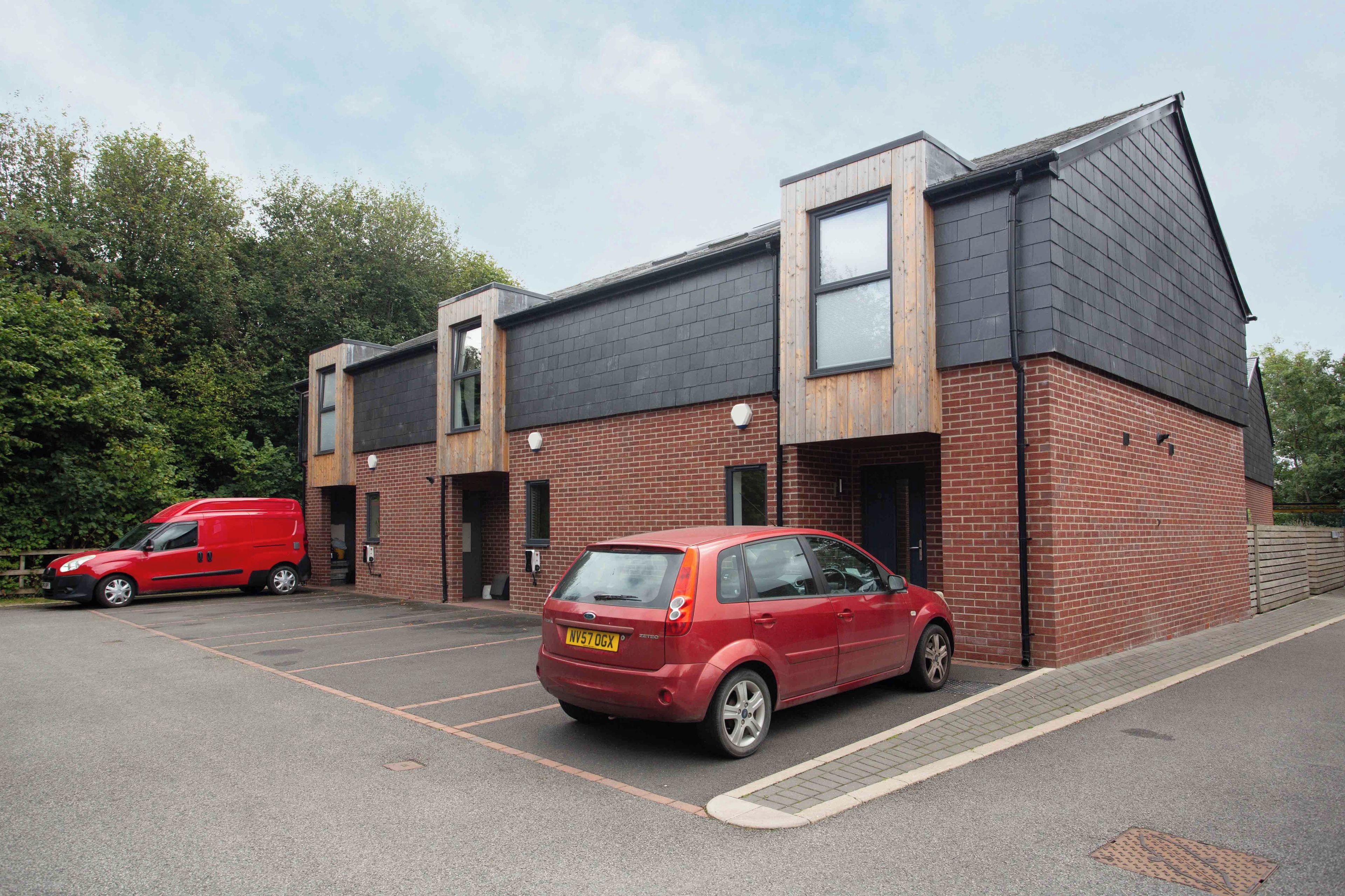 A two-story building with a brick facade, a flat roof, and a parking area with two cars.