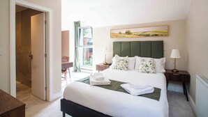 Un dormitorio con una cama grande, una ventana con vistas, un cuadro en la pared y una puerta que conduce a otra habitación.