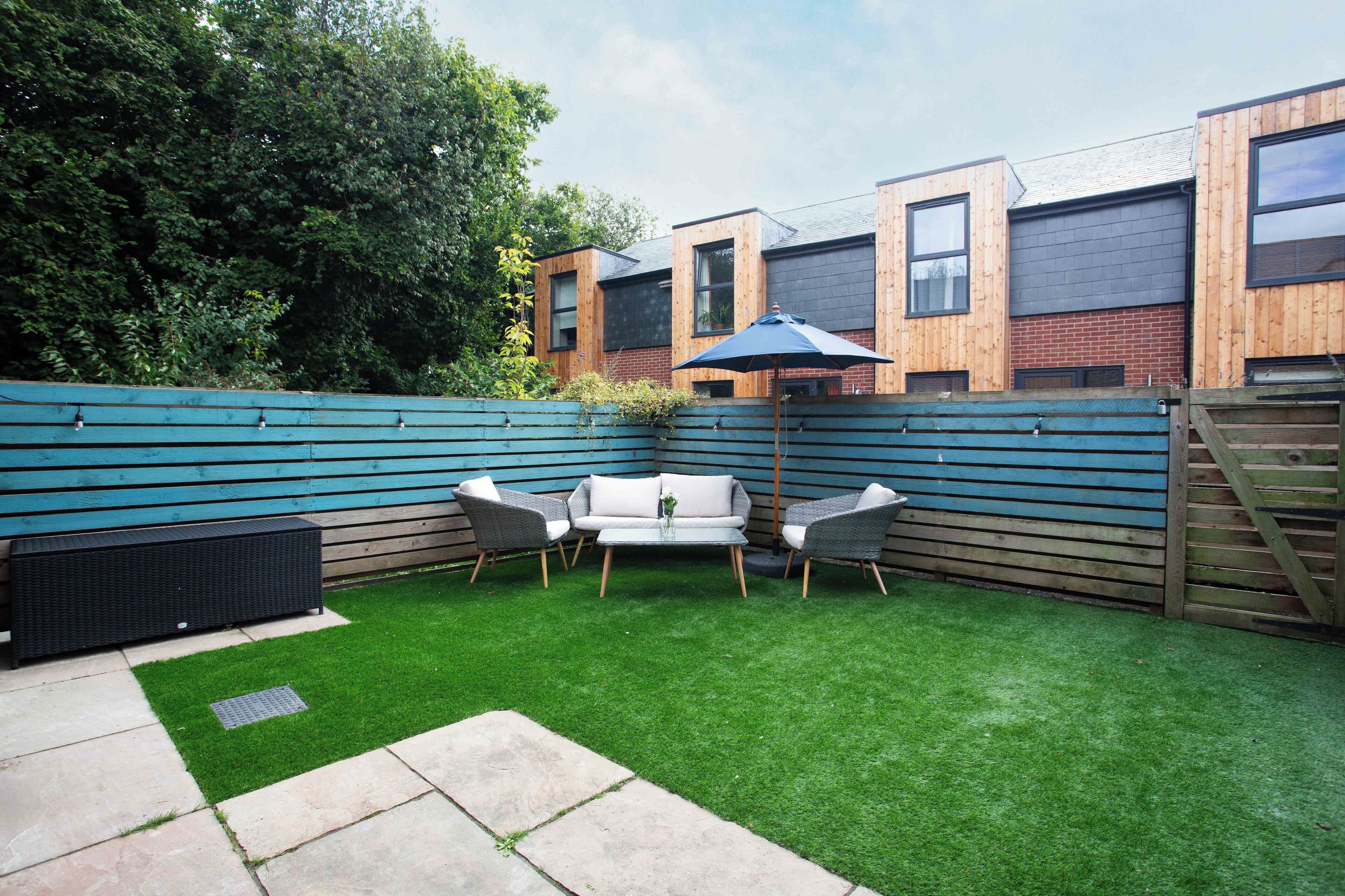 A backyard with artificial grass, a seating area with two chairs and a table, and a wooden fence.