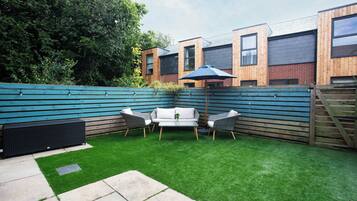A backyard with artificial grass, a seating area with two chairs and a table, and a wooden fence.