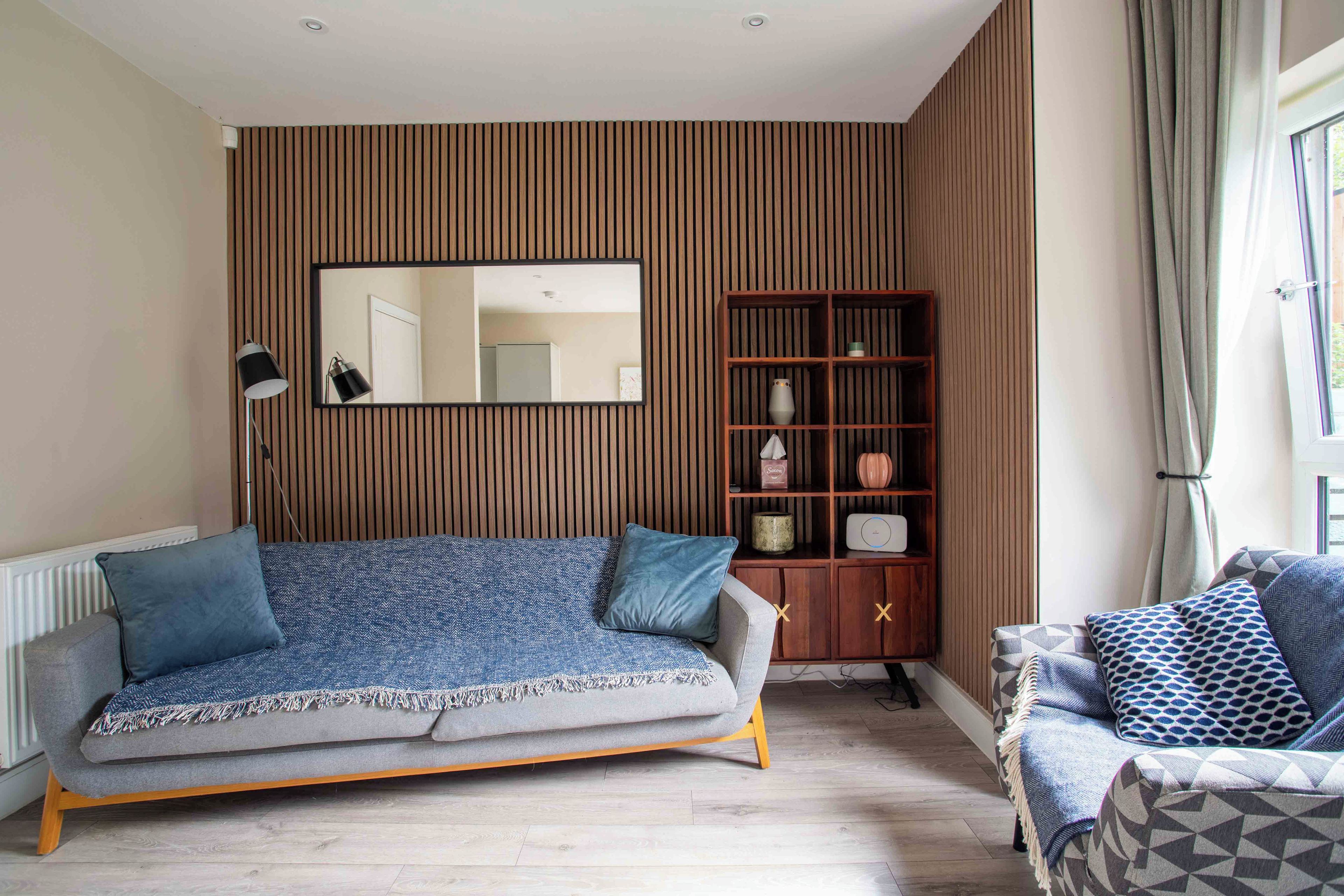 A living room with a sofa, a side table, a mirror, and a wooden panel wall.