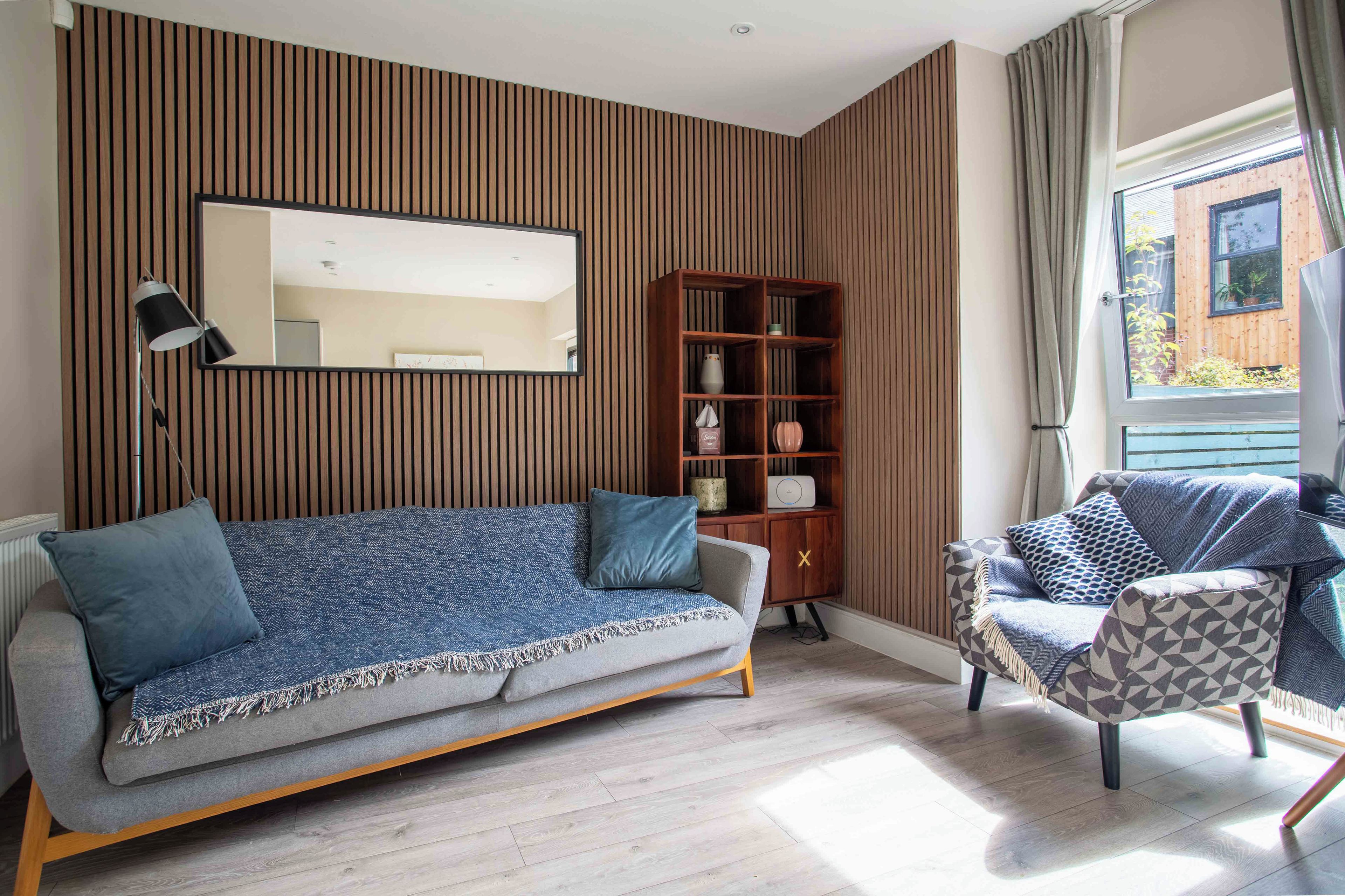 A modern living room with a sofa, a side table, a bookshelf, and a window with curtains.