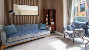 A modern living room with a sofa, a side table, a bookshelf, and a window with curtains.