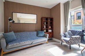 A modern living room with a sofa, a side table, a bookshelf, and a window with curtains.