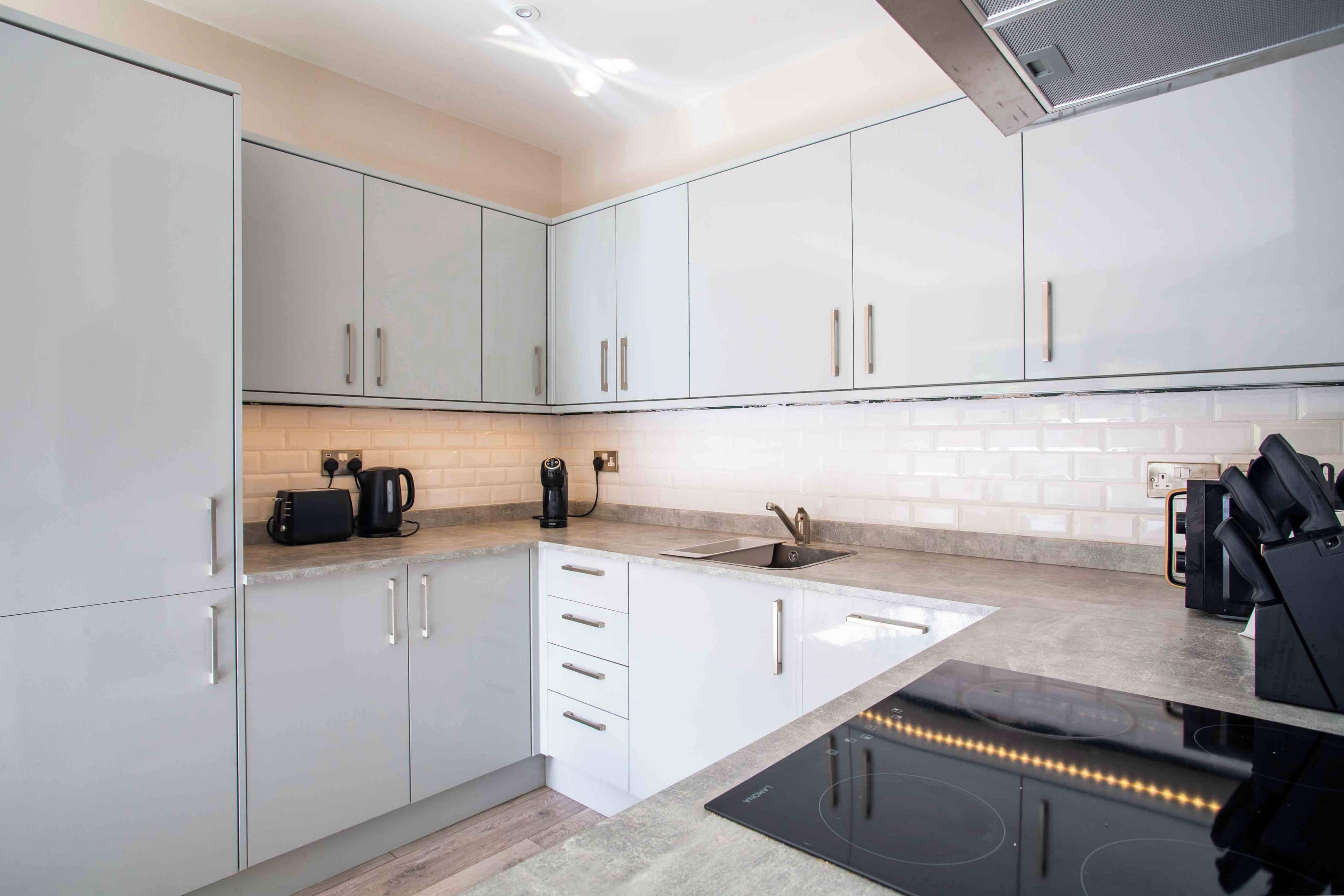 A modern kitchen with white cabinets, a built-in oven, a coffee maker, and a knife block.