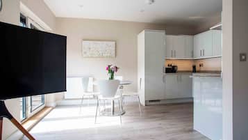 A modern kitchen with white cabinets, a dining area with a white table and chairs, and a flat-screen TV mounted on a wall.