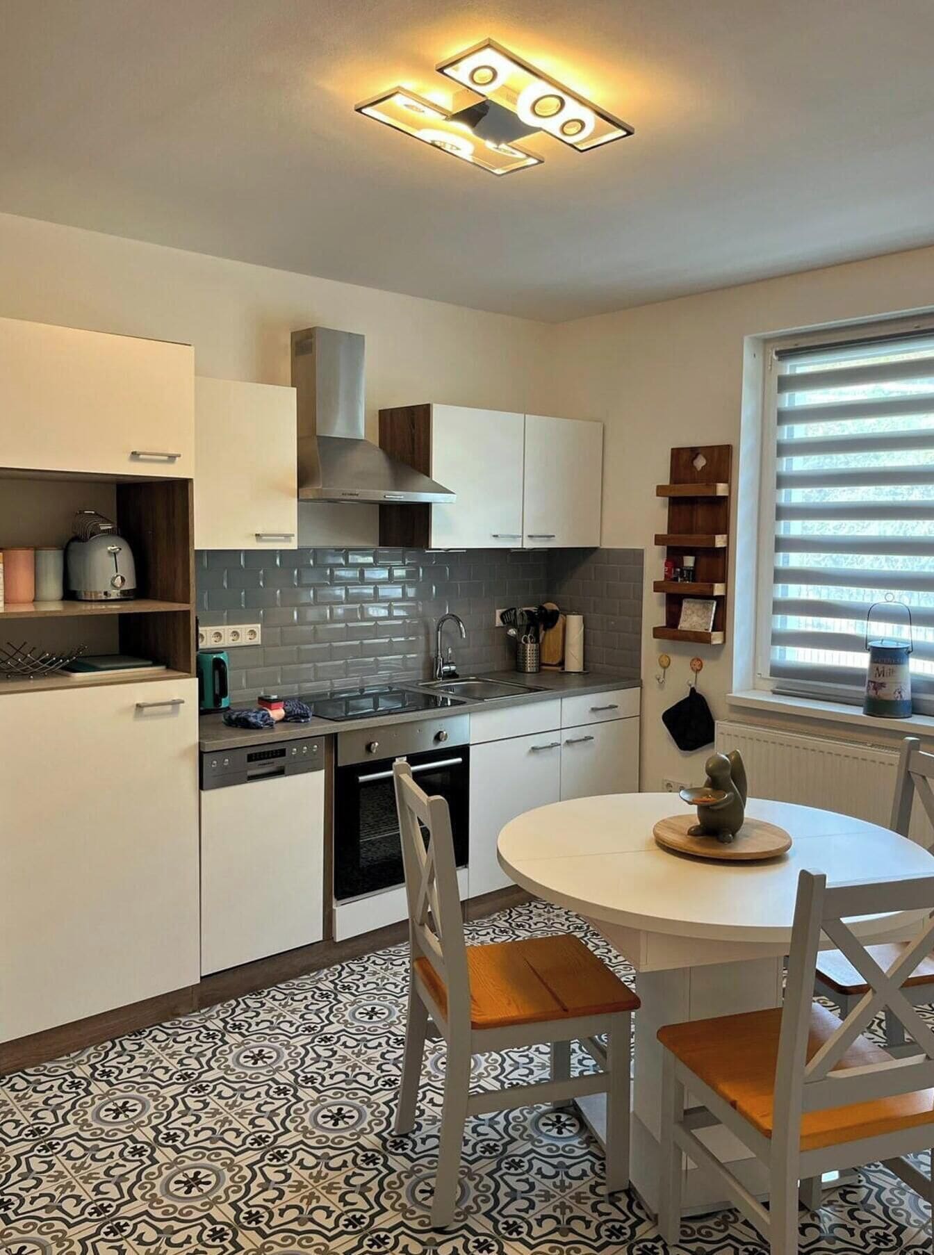 Een moderne keuken met witte kasten, een inbouwoven en een ronde eettafel met stoelen.