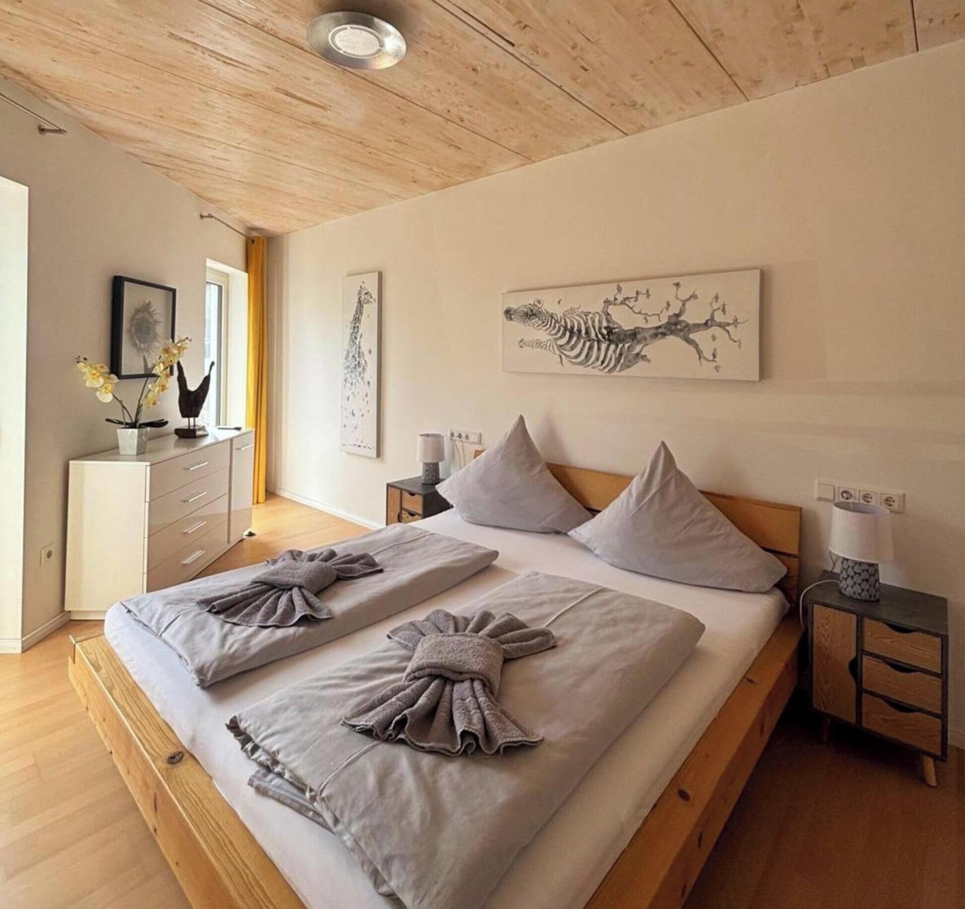 Een slaapkamer met een houten bed, twee nachtkastjes, een bijzettafeltje en kunstwerken aan de wanden.