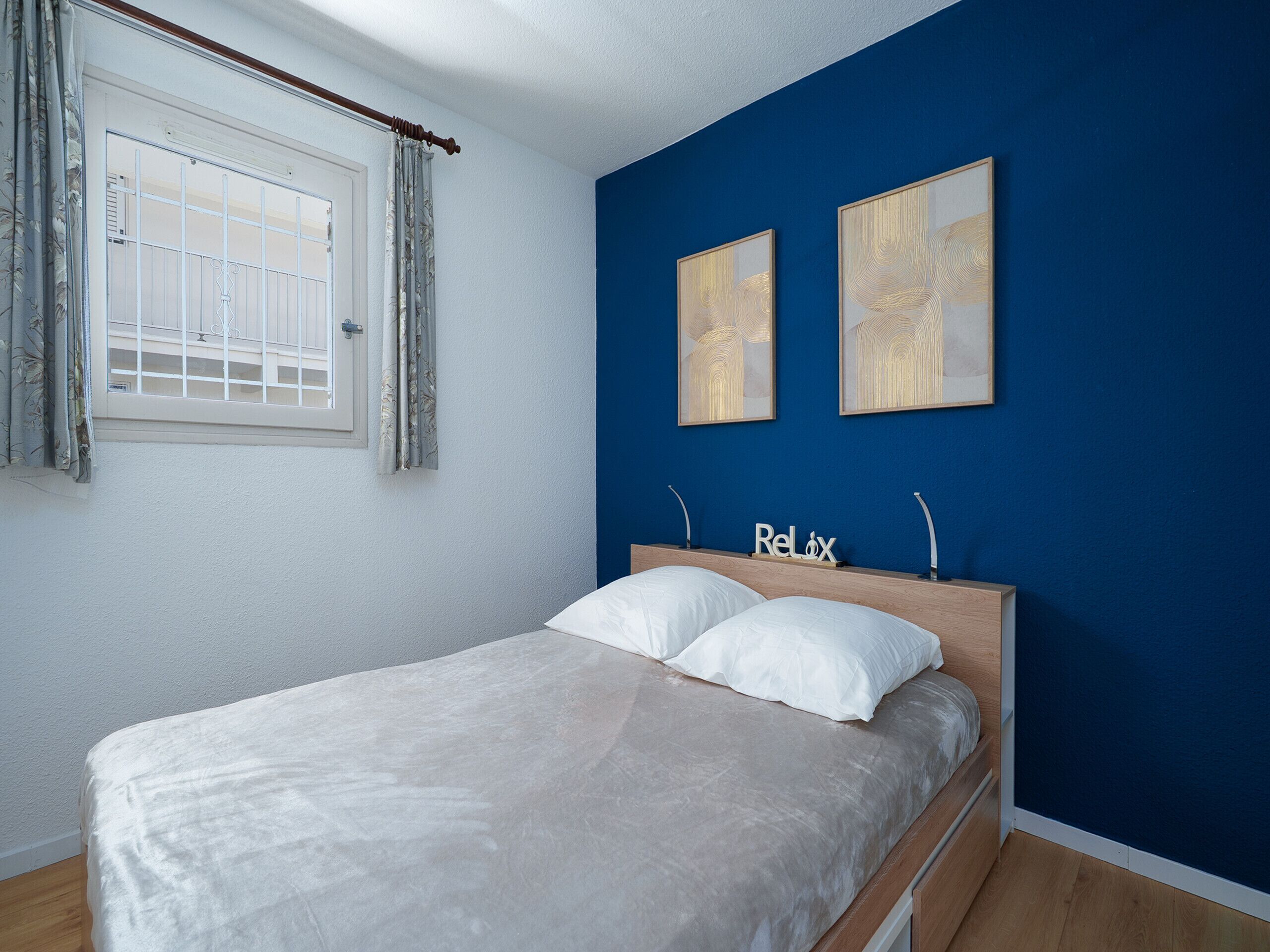 Un dormitorio con cama, una ventana con cortinas y dos obras de arte colgadas en la pared.