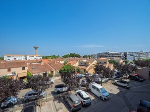 A parking lot with multiple cars, a white van, and a building with a red-tiled roof in the background. - Air-conditioned apartment with a garage and Wi-Fi (Le Grau-du-Roi)