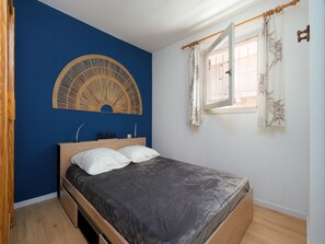 A bedroom with a bed, a wall-mounted decorative item, a window with curtains, and a wooden floor. - Air-conditioned apartment with a garage and Wi-Fi (Le Grau-du-Roi)