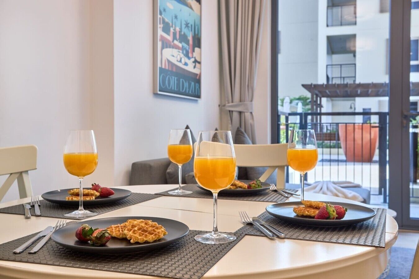 Ein Frühstückstisch mit Waffeln, Erdbeeren, Orangensaftgläsern und Blick auf ein Gebäude durch ein Fenster.