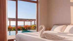Ein Schlafzimmer mit einem großen Bett, einem schwanenförmigen Kopfkissen und Blick auf einen Infinity-Pool und Außenbereich.