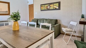 Un comedor con una mesa de madera, sillas blancas, un sofá verde y un cuadro en la pared.