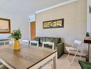 Ein Essbereich mit einem Holztisch, weißen Stühlen, einer grünen Couch und einem Bild an der Wand.