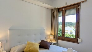 Una habitación de hotel con cama, mesita de noche, lámpara, ventana con cortinas y toallas sobre la cama.