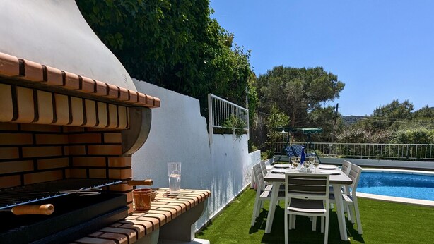 Una parrilla con diseño de ladrillo, una piscina y un comedor con sillas blancas.