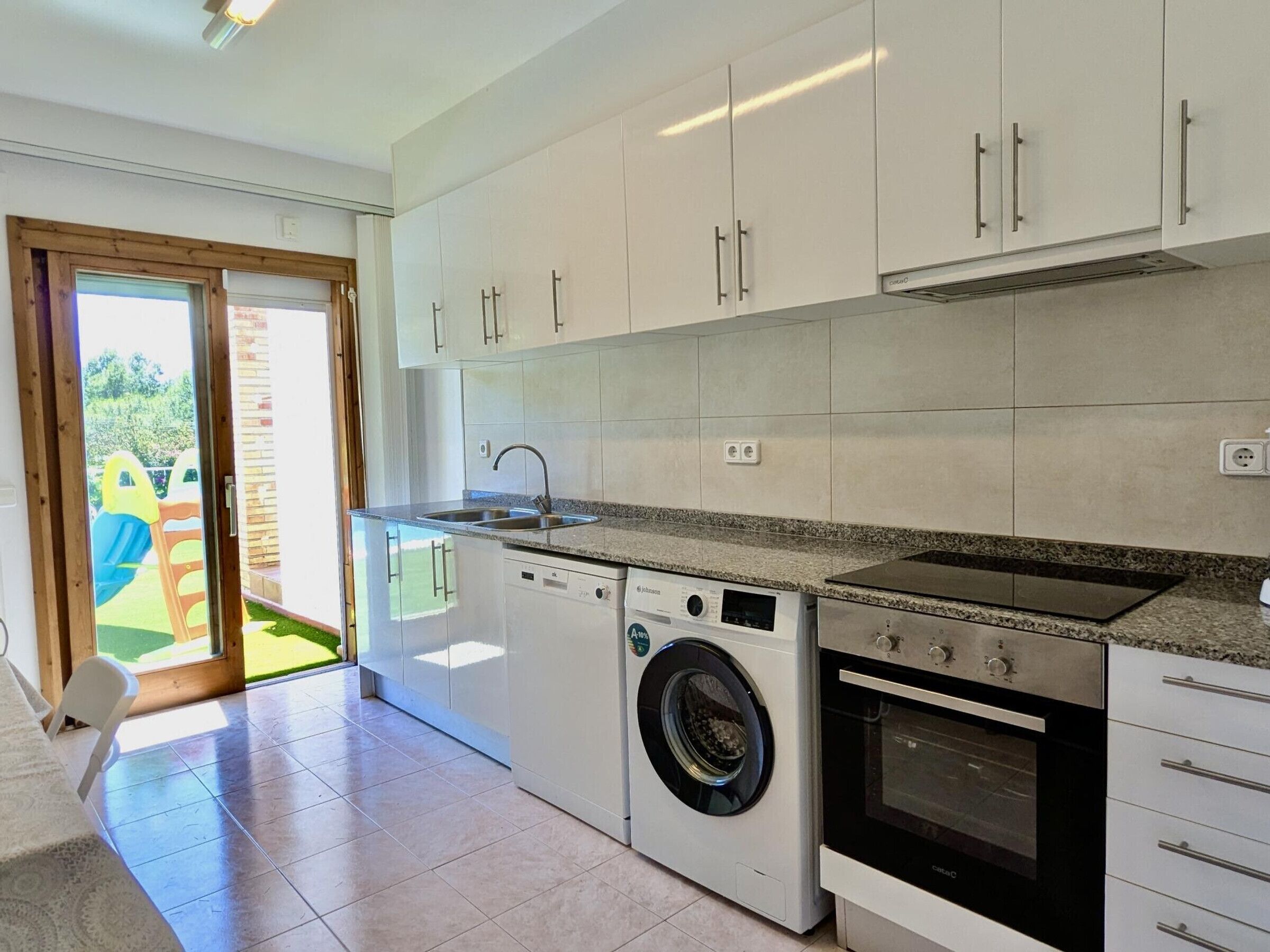 Une cuisine moderne avec des meubles blancs, un lave-linge encastré et un four.