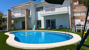 Una piscina con tobogán, rodeada de césped, y un edificio con balcones y terraza.