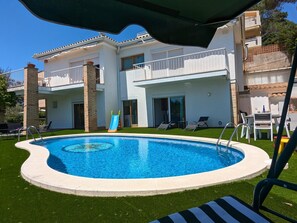 Ein Schwimmbecken mit Wasserrutsche, umgeben von einer Rasenfläche, und ein Gebäude mit Balkonen und einer Terrasse.