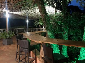 An outdoor seating area with a wooden bar and wicker chairs, surrounded by greenery and a stone wall. - Bungalow - 4 guests, pets welcome (ALBITRECCIA)