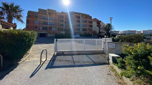 En grind leder in till en bostadsbyggnad med flera våningar och balkonger. Himlen är klar och en bil står parkerad.