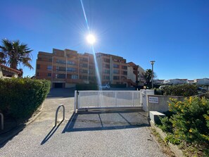 A gated entrance to a residential building with multiple floors and balconies, a clear sky, and a parked car. - Air-conditioned apartment, sea view - 4 guests (Port Leucate)