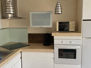 A compact kitchen with a microwave, oven, and a coffee maker on the countertop. - Air-conditioned apartment, sea view - 4 guests (Port Leucate)