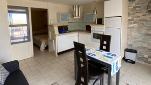 A compact kitchen with a dining area, a microwave, a refrigerator, and a window overlooking a balcony.