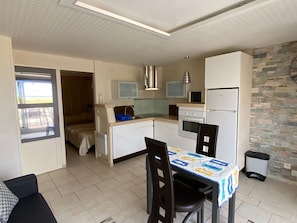 A compact kitchen with a dining area, a microwave, a refrigerator, and a window overlooking a balcony. - Air-conditioned apartment, sea view - 4 guests (Port Leucate)