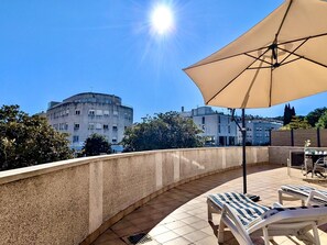 Eine Dachterrasse mit Lounge-Möbeln, Sonnenschirm und Blick auf die umliegenden Gebäude.