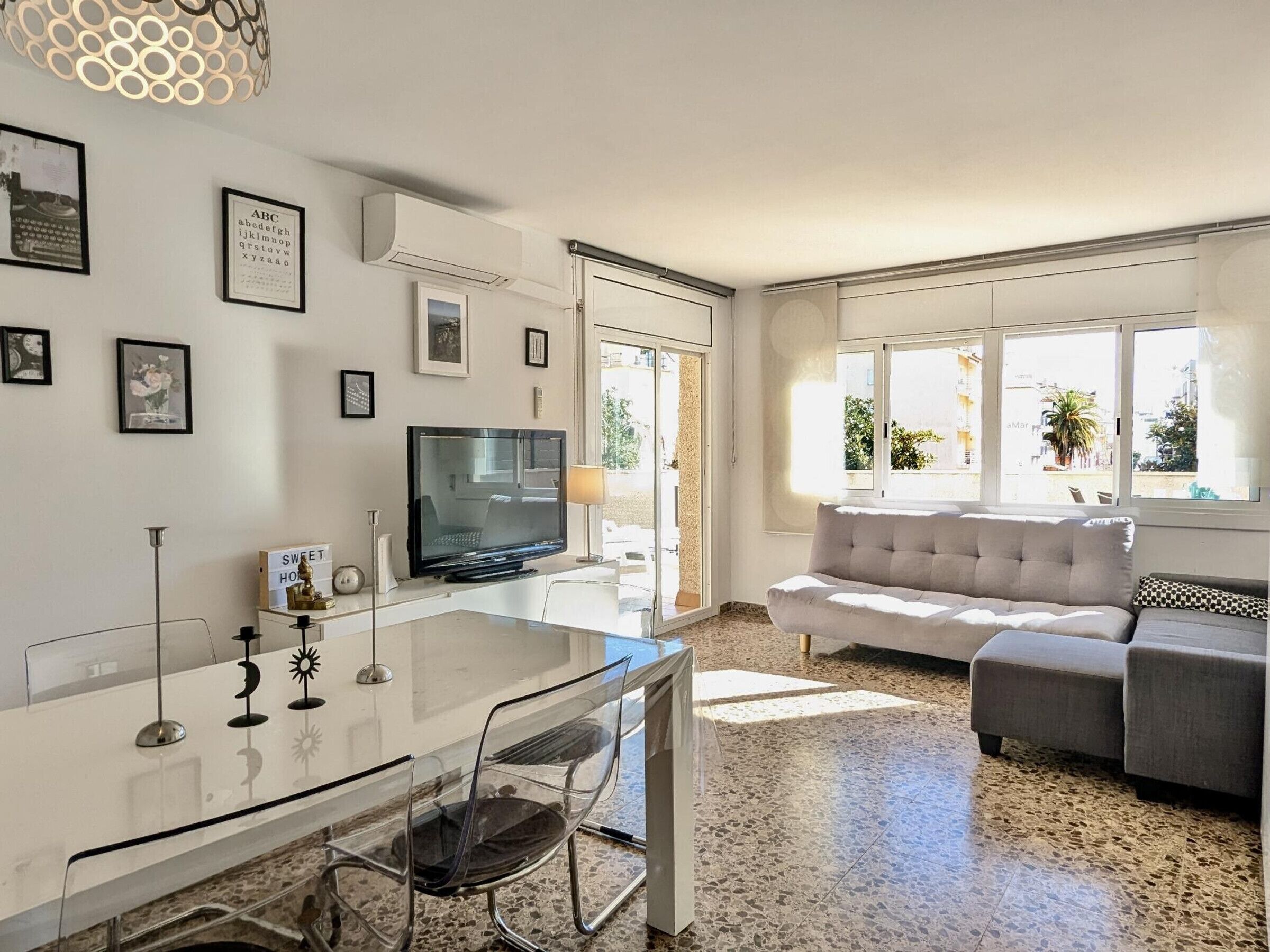 A modern living room with a flat-screen TV, a glass dining table, and a sofa.
