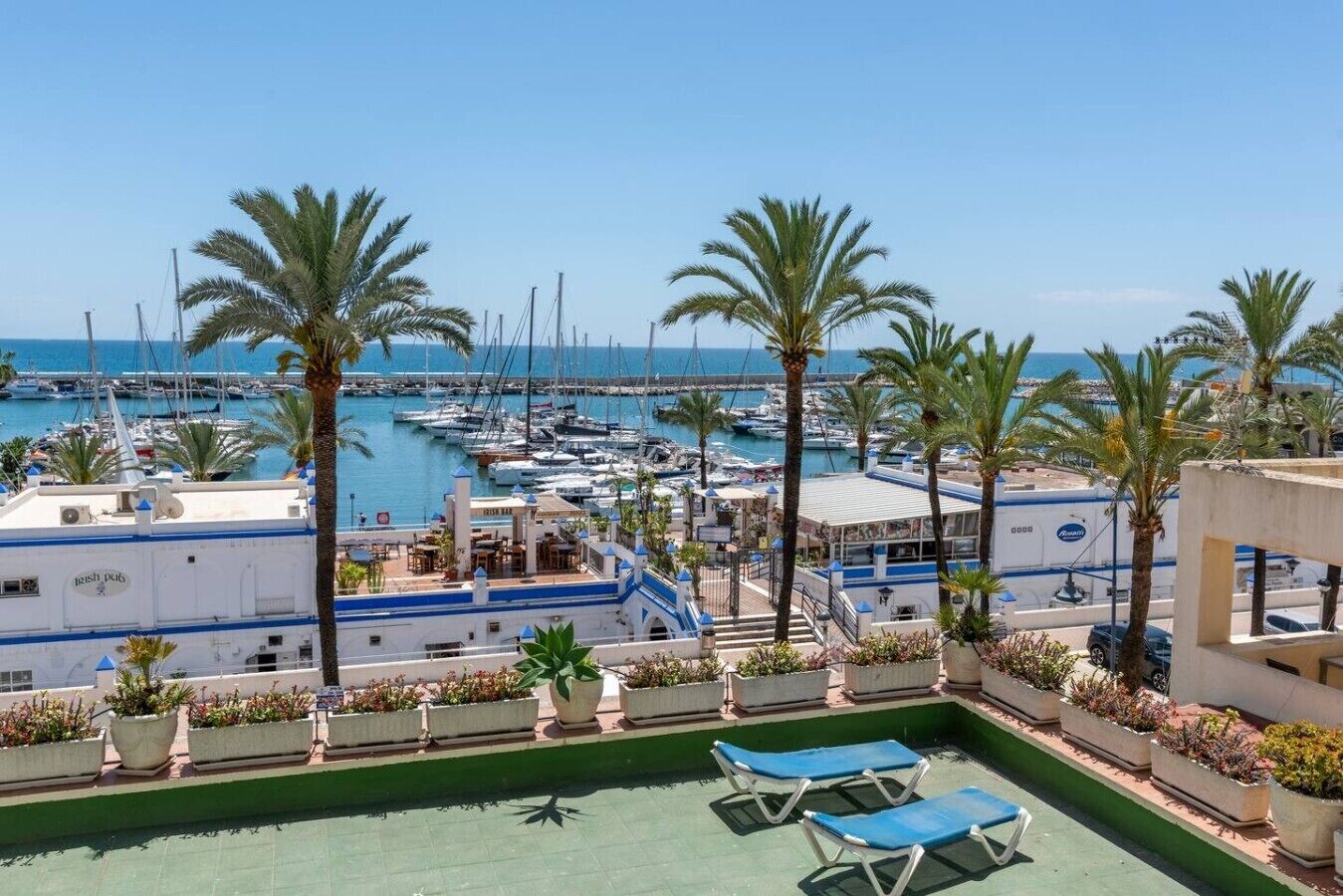 A marina with boats, palm trees, and a building with outdoor seating.