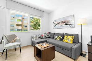 A modern living room with a grey sofa, a small wooden coffee table, and a white armchair. - Apartment with a Terrace and Swimming Pools in El Puerto (Estepona)