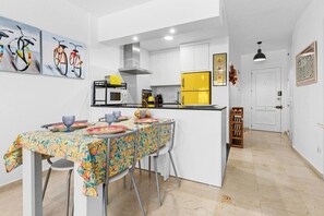 A compact kitchen with white cabinets, a yellow refrigerator, and a dining area with a floral tablecloth. - Apartment with a Terrace and Swimming Pools in El Puerto (Estepona)