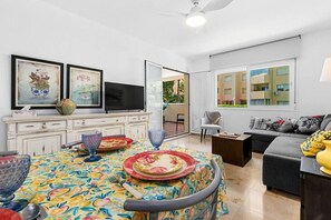 A dining area with a table set for two, a television, and a sofa in a bright living room with large windows. - Apartment with a Terrace and Swimming Pools in El Puerto (Estepona)