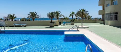 Une piscine à l’eau d’un bleu cristallin, entourée de chaises longues et de palmiers, avec un bâtiment visible au loin.