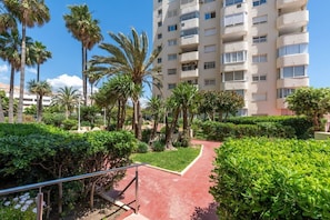 A multi-story residential building with balconies, surrounded by well-maintained greenery and a red pathway. - Apartment with a Terrace and Swimming Pools in El Puerto (Estepona)