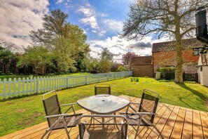 Eine Terrasse im Freien mit Tisch und Stühlen, umgeben von einem weißen Zaun, Bäumen und einem Backsteinhaus.