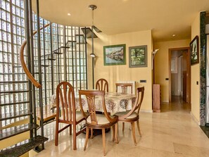 A dining area with a table set for four, surrounded by wooden chairs, with a view of a cityscape through a large window. - House with private pool, parking - 8 guests (Tossa de Mar)