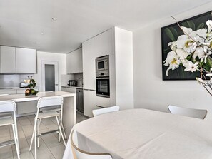 A modern kitchen with white cabinetry, a built-in oven, and a dining area with a table and chairs. - Spacious apartment, panoramic view - 9 guests (Tossa de Mar)