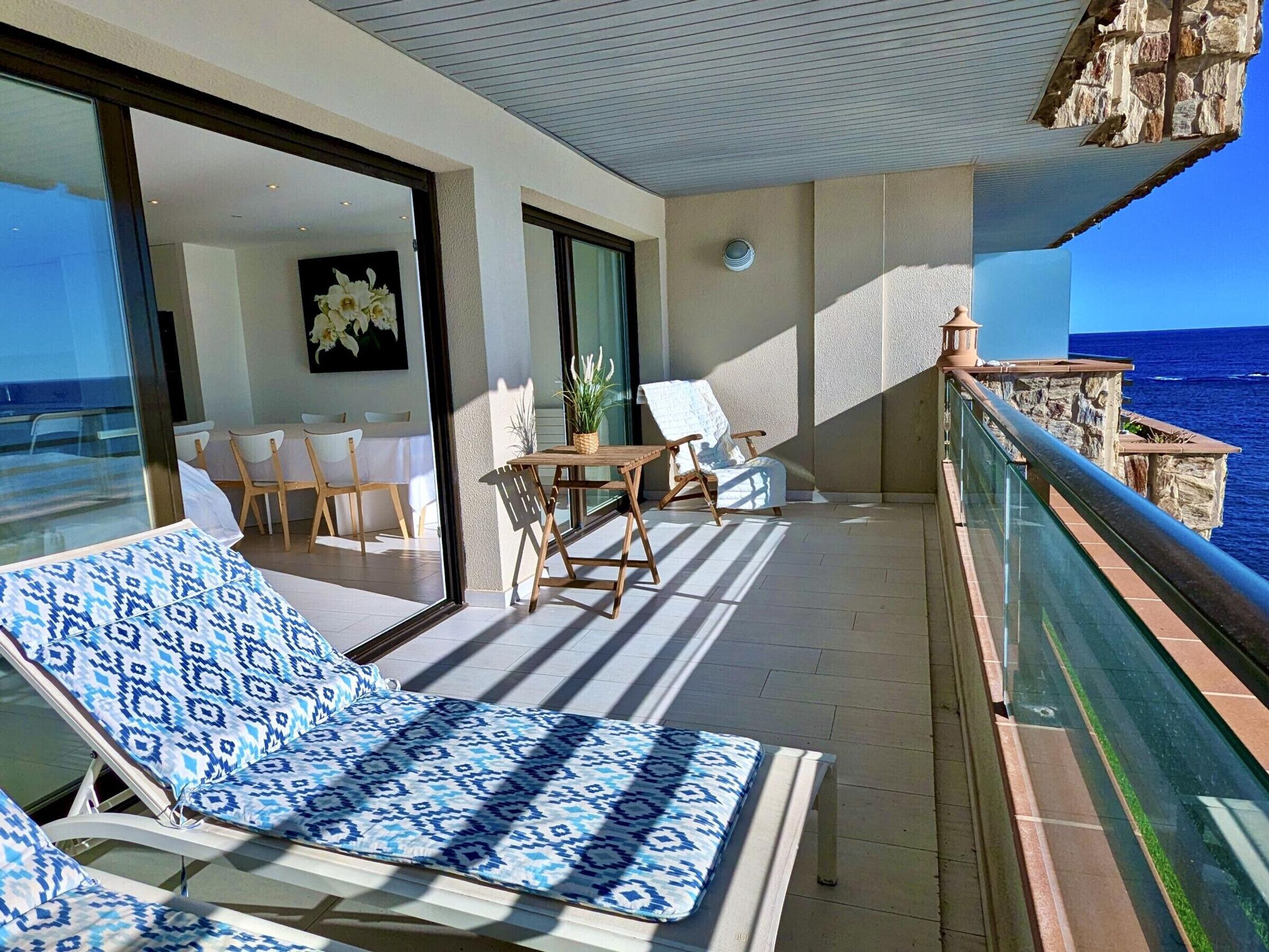 A balcony with a view of the sea, a dining area, and a lounge with patterned cushions.