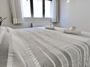A hotel room with a large bed, a window with curtains, and a radiator. - Spacious apartment, panoramic view - 9 guests (Tossa de Mar)