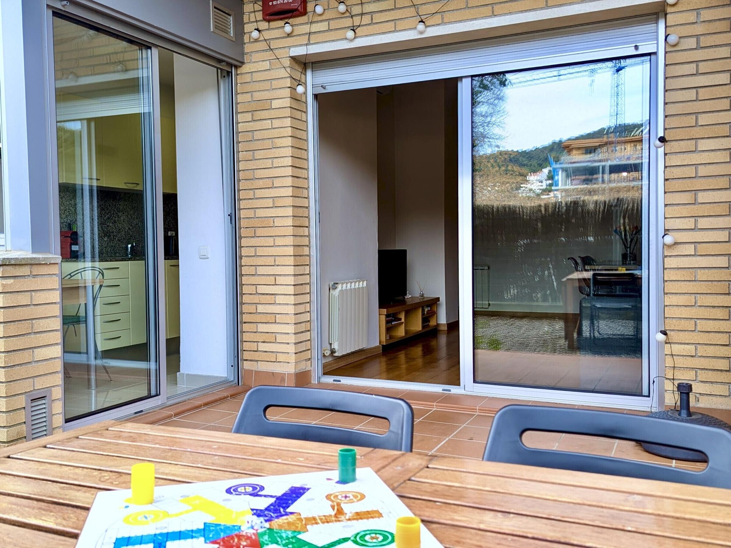 Un patio con mesa y sillas, un portón corredizo que da a un balcón y vistas a un edificio con una fuente.