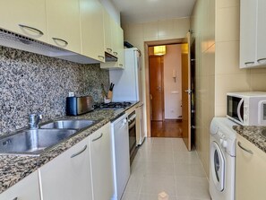 Eine kleine Küche mit Granit Arbeitsplatten, Spüle aus Edelstahl, weißen Schränken, einer Mikrowelle und einer Waschmaschine.