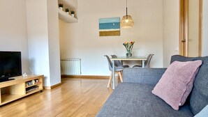Ett vardagsrum med en soffa, en tv, ett matbord med stolar, en hänglampa och en tavla på väggen.